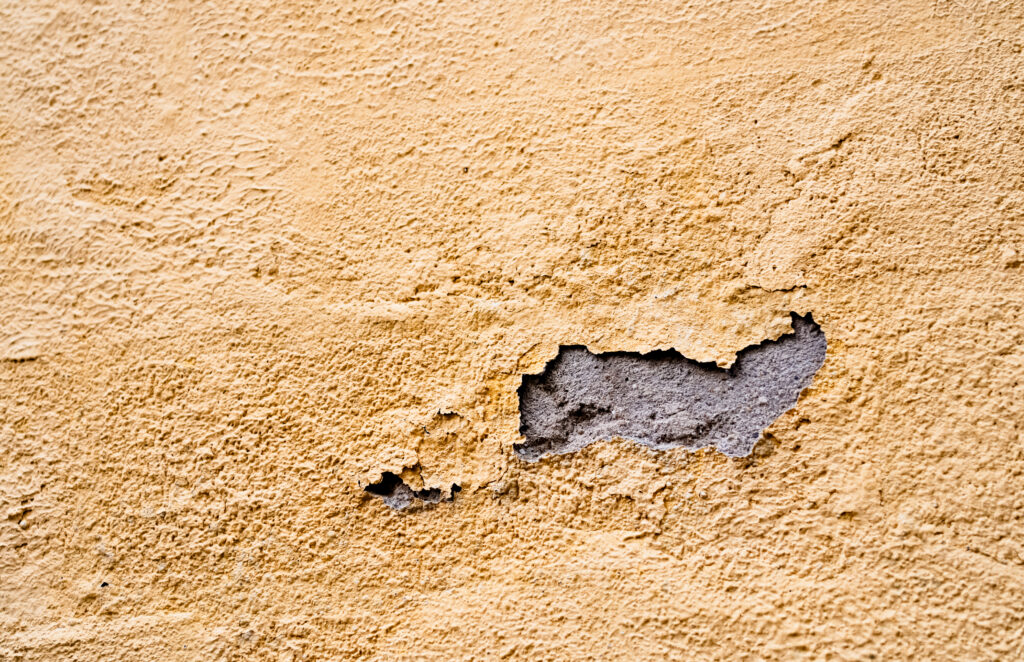 Hole and surface damage in exterior stucco before repair